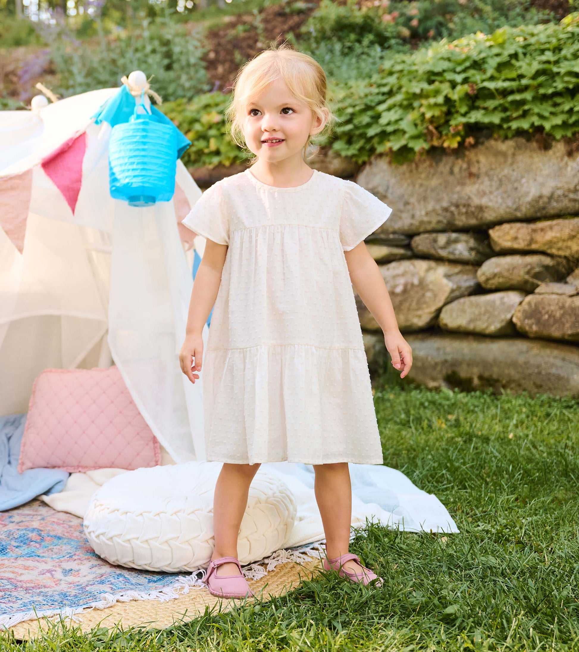 Toddler girl wearing a pearl Swiss dot dress with short flutter sleeves and a tiered skirt outdoors
