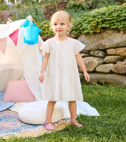 Toddler girl wearing a pearl Swiss dot dress with short flutter sleeves and a tiered skirt outdoors