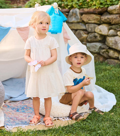 Toddler wearing an ivory Swiss dot puff sleeve dress standing beside another child outdoors