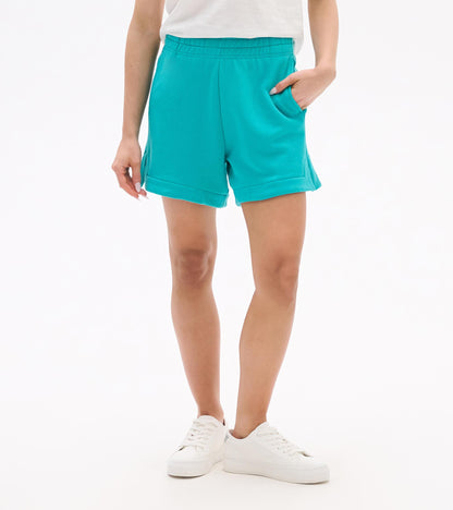 Turquoise pull-on shorts with elastic waistband, side pockets, and cuffed hems, worn with white sneakers