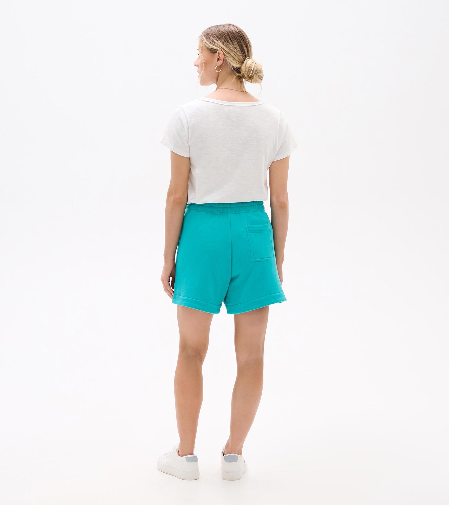 Back view of turquoise shorts with elastic waistband, rolled hems, and back pocket, worn with a white T-shirt and sneakers