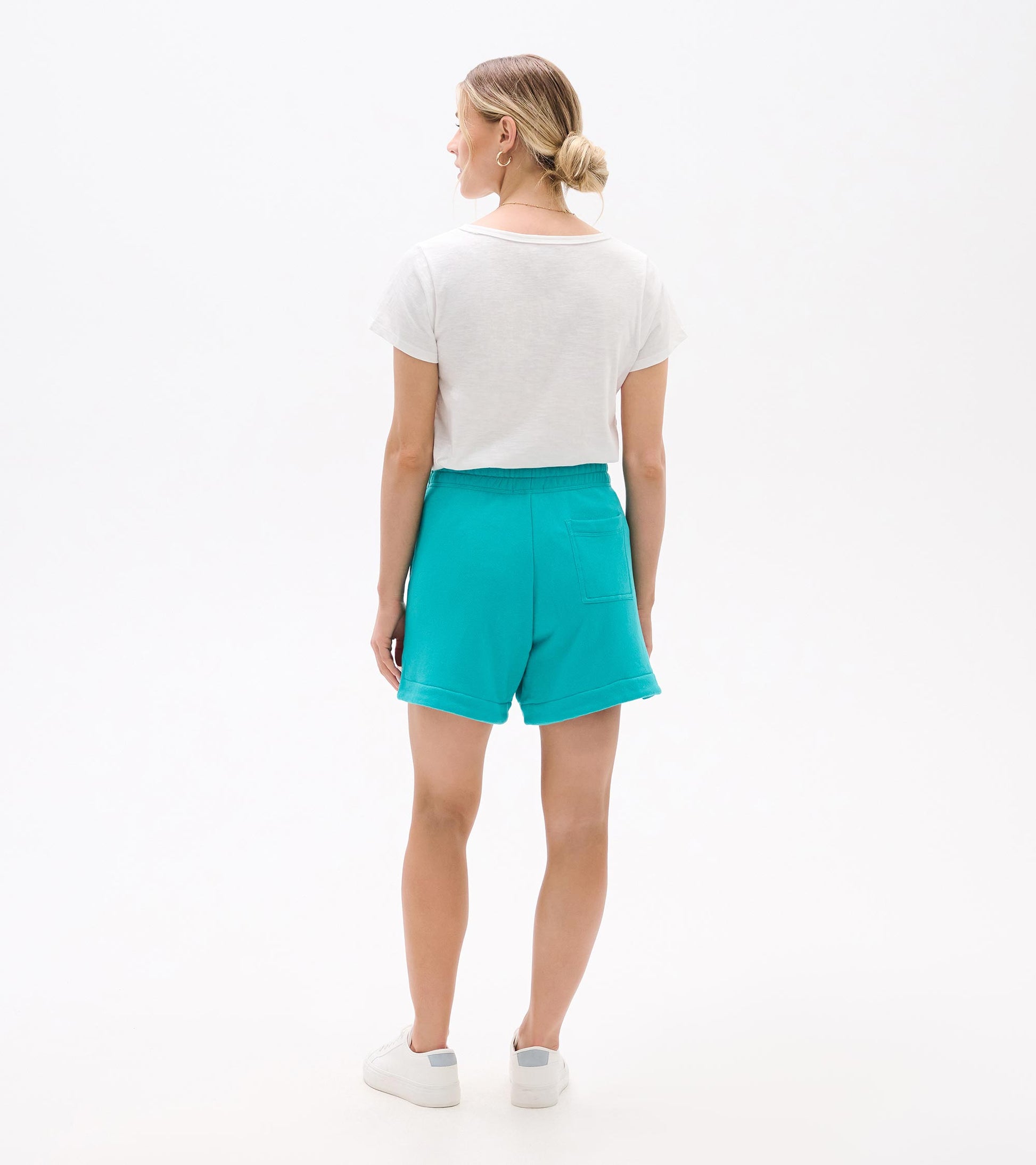 Back view of turquoise shorts with elastic waistband, rolled hems, and back pocket, worn with a white T-shirt and sneakers