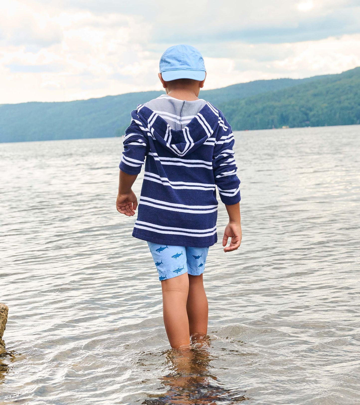 Back view of a boy wearing a navy and white striped hooded long-sleeve cover-up at the beach