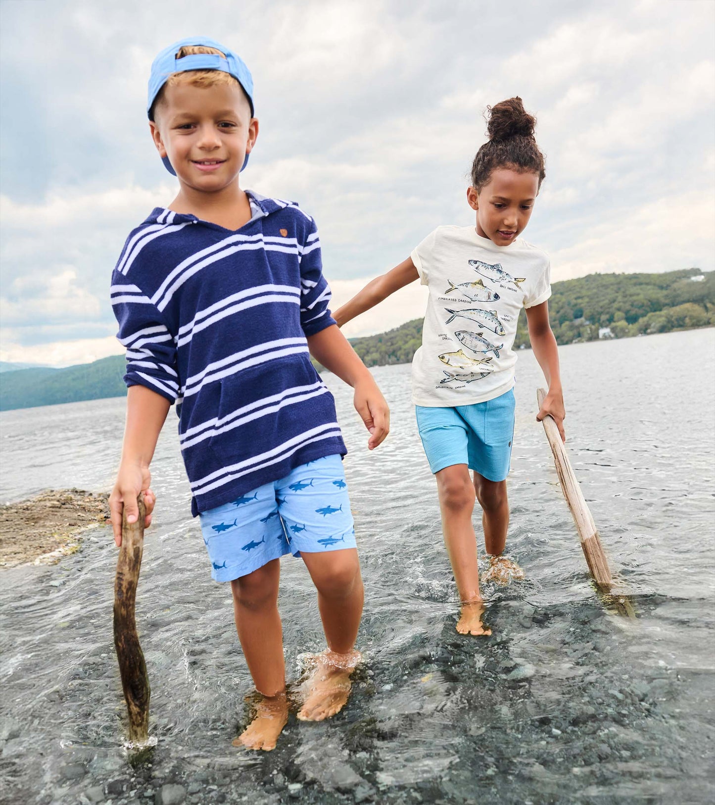 Boy wearing navy striped hooded long-sleeve cover-up with light blue shorts, front view, standing in water