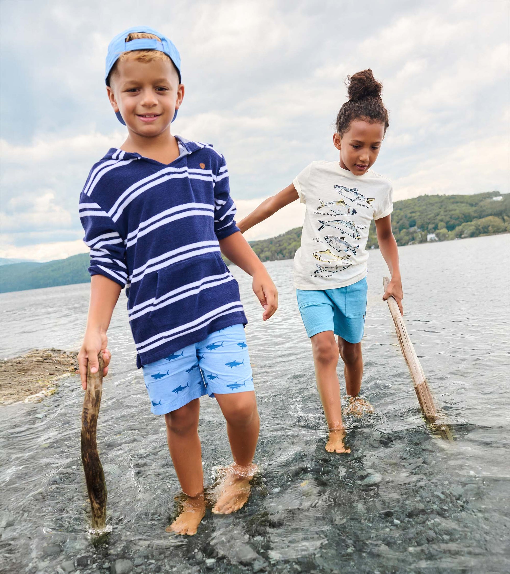 Boy wearing navy striped hooded long-sleeve cover-up with light blue shorts, front view, standing in water