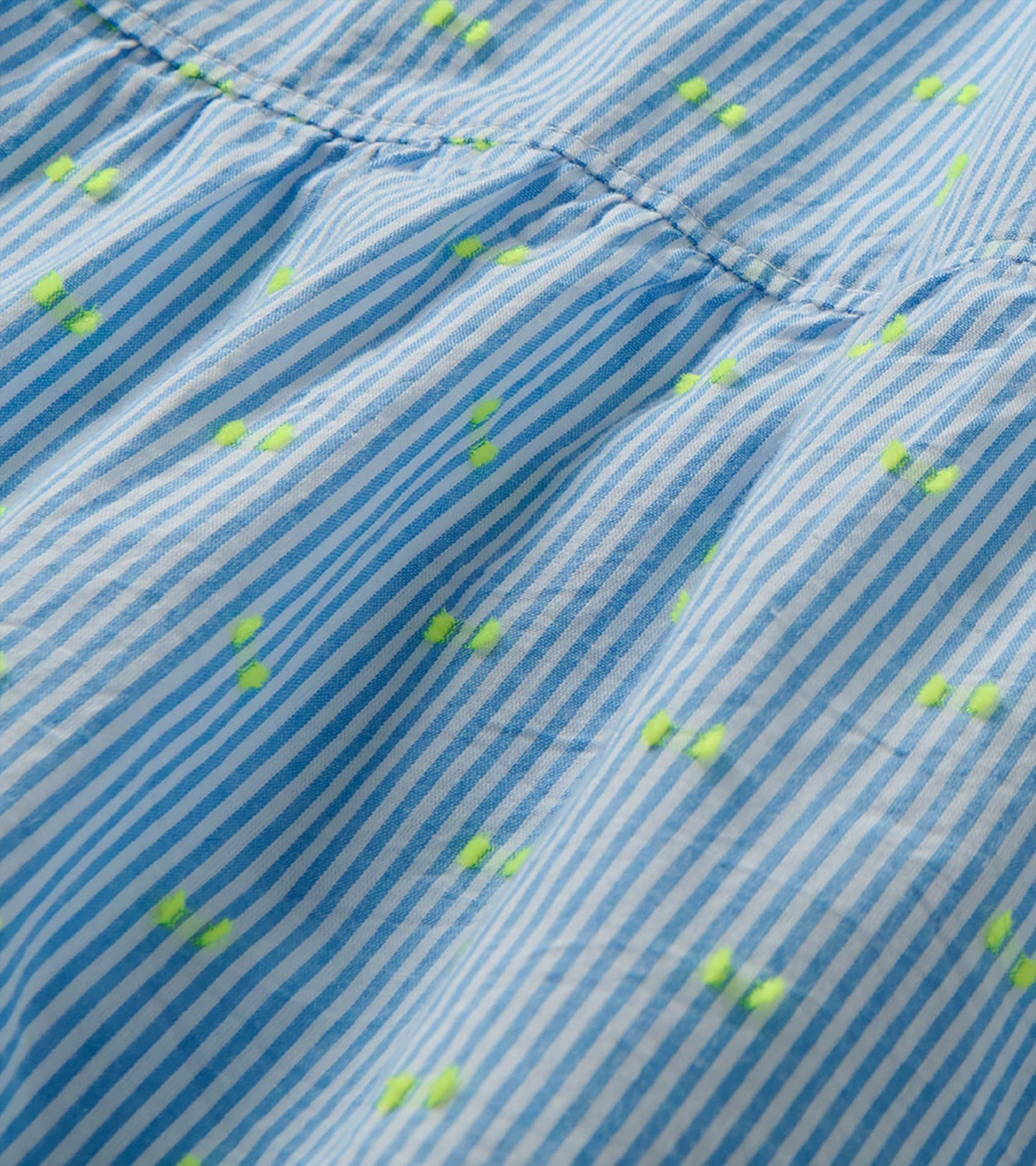 Close-up of blue and white striped dress fabric with neon yellow dots and a gathered seam