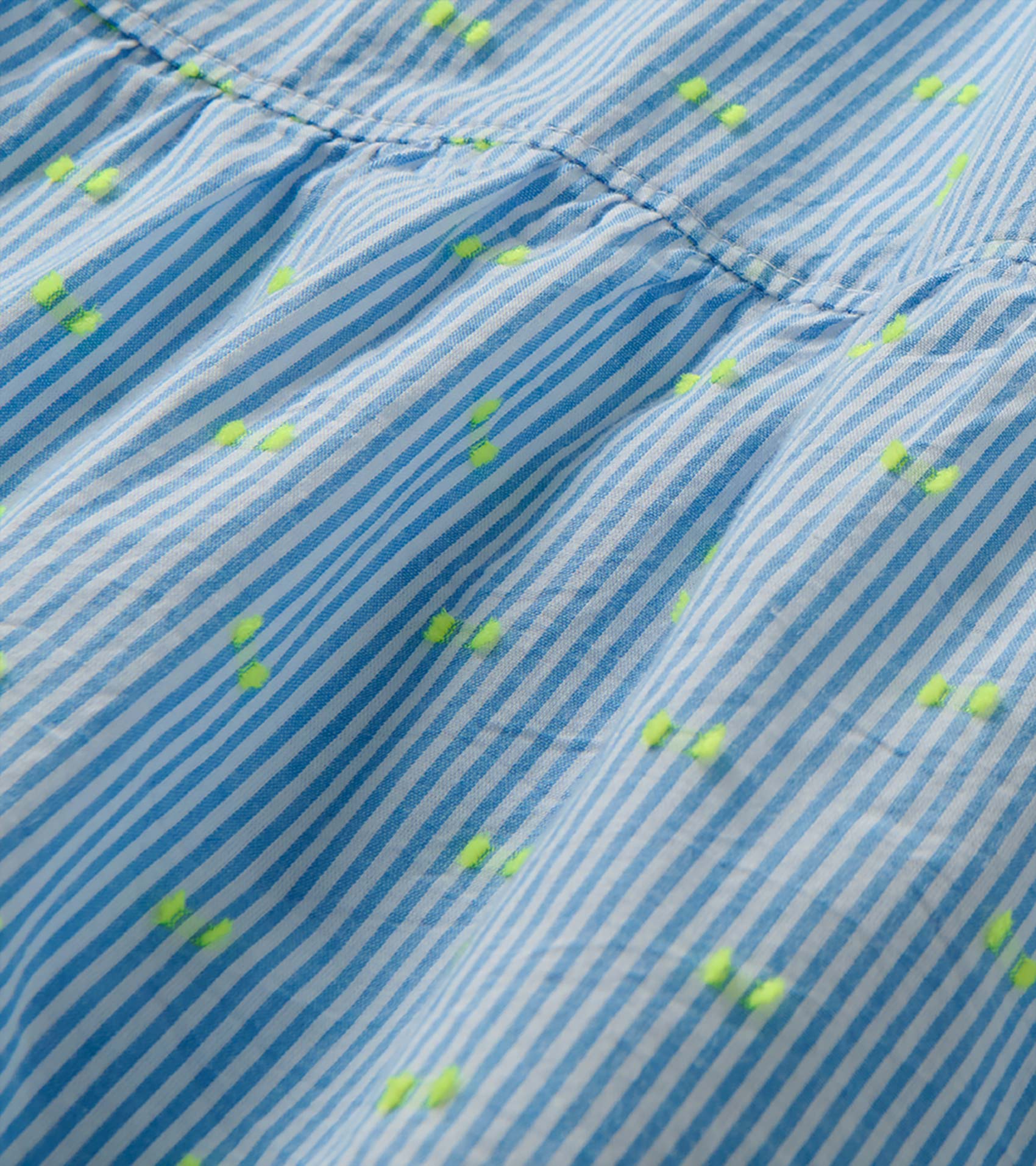 Close-up of blue and white striped dress fabric with neon yellow dots and a gathered seam