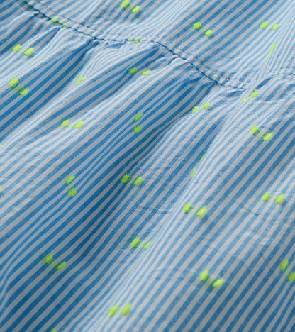 Close-up of blue and white striped dress fabric with neon yellow dots and a gathered seam