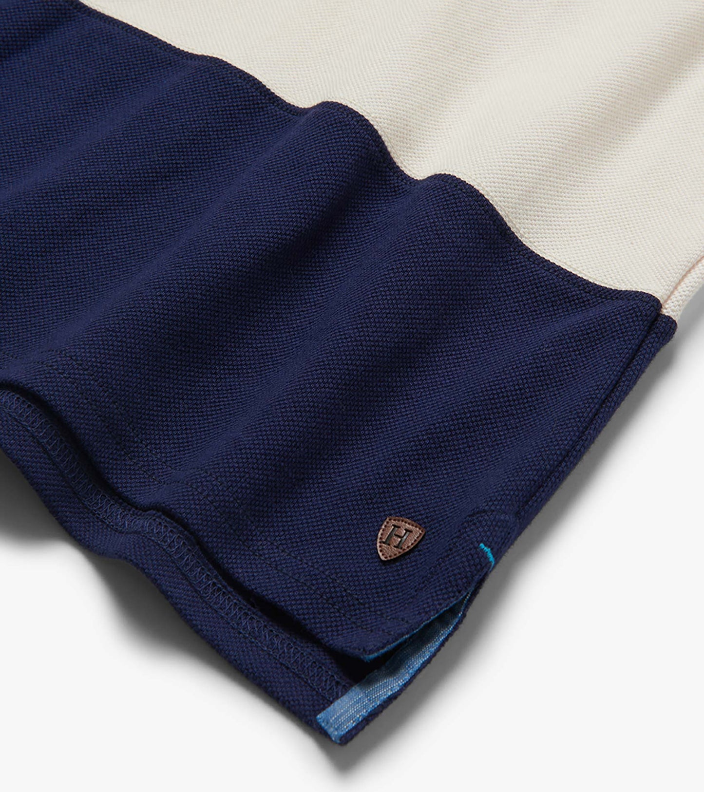 Folded navy and cream color block polo shirt with textured knit fabric and small chest logo patch
