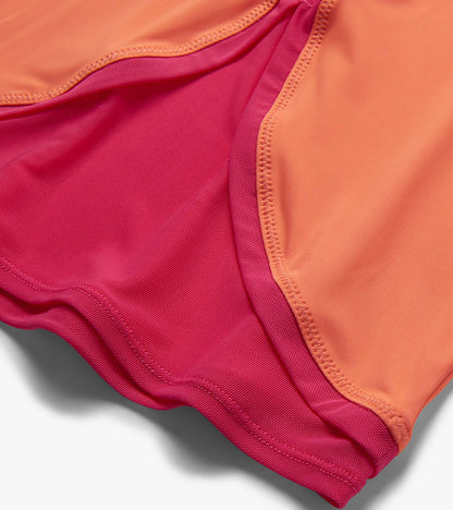 Close-up of coral and magenta mesh-trimmed T-shirt hem with curved stitching and layered fabric detail