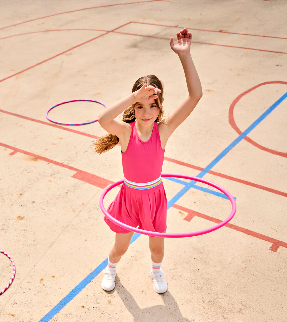 Girl wearing bright pink active dress with pleated skirt and striped waistband, hula hoop at waist