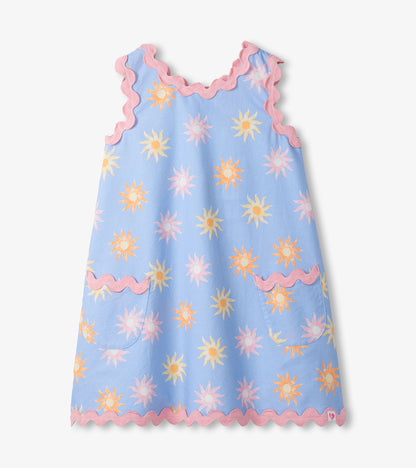 Light blue girls pinafore dress with pastel sun print, pink scalloped trim, and front patch pockets