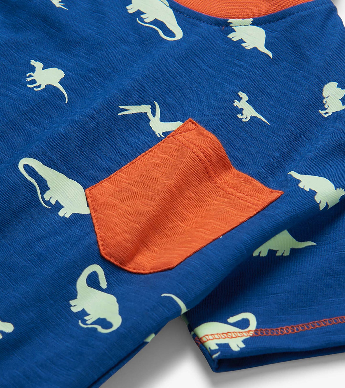 Blue toddler T-shirt with white dinosaur print and orange chest pocket, close-up view