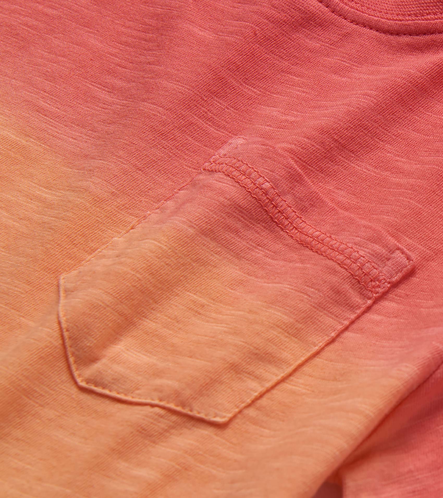 Close-up of a coral and peach gradient knit T-shirt pocket with stitched trim and heathered texture