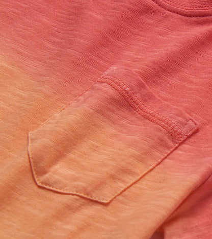 Close-up of a coral and peach gradient knit T-shirt pocket with stitched trim and heathered texture