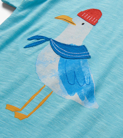 Close-up of light blue fabric with embroidered seagull wearing a red hat and blue scarf