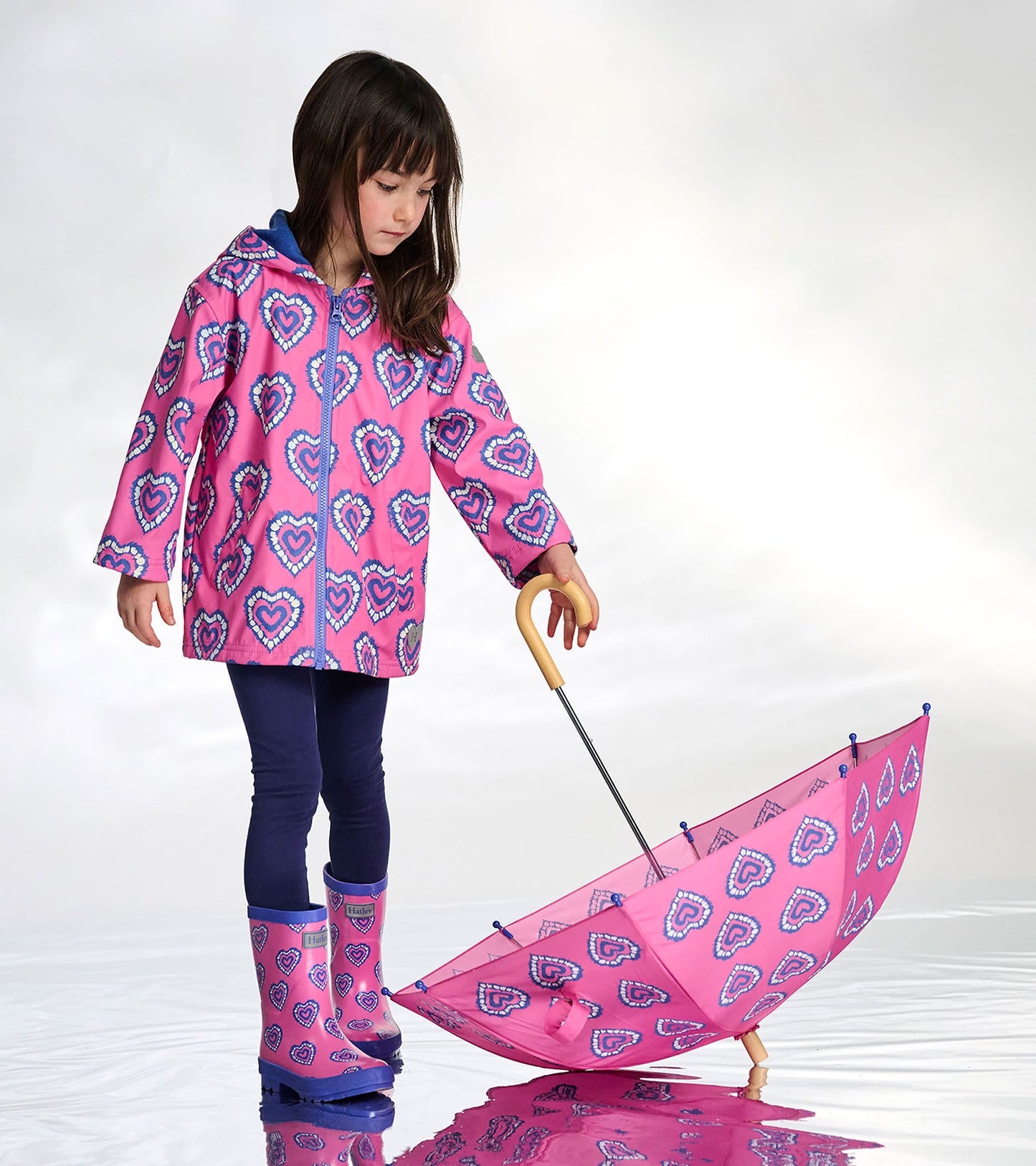 Pink kids umbrella with blue heart pattern, wooden handle, shown open with a child holding it