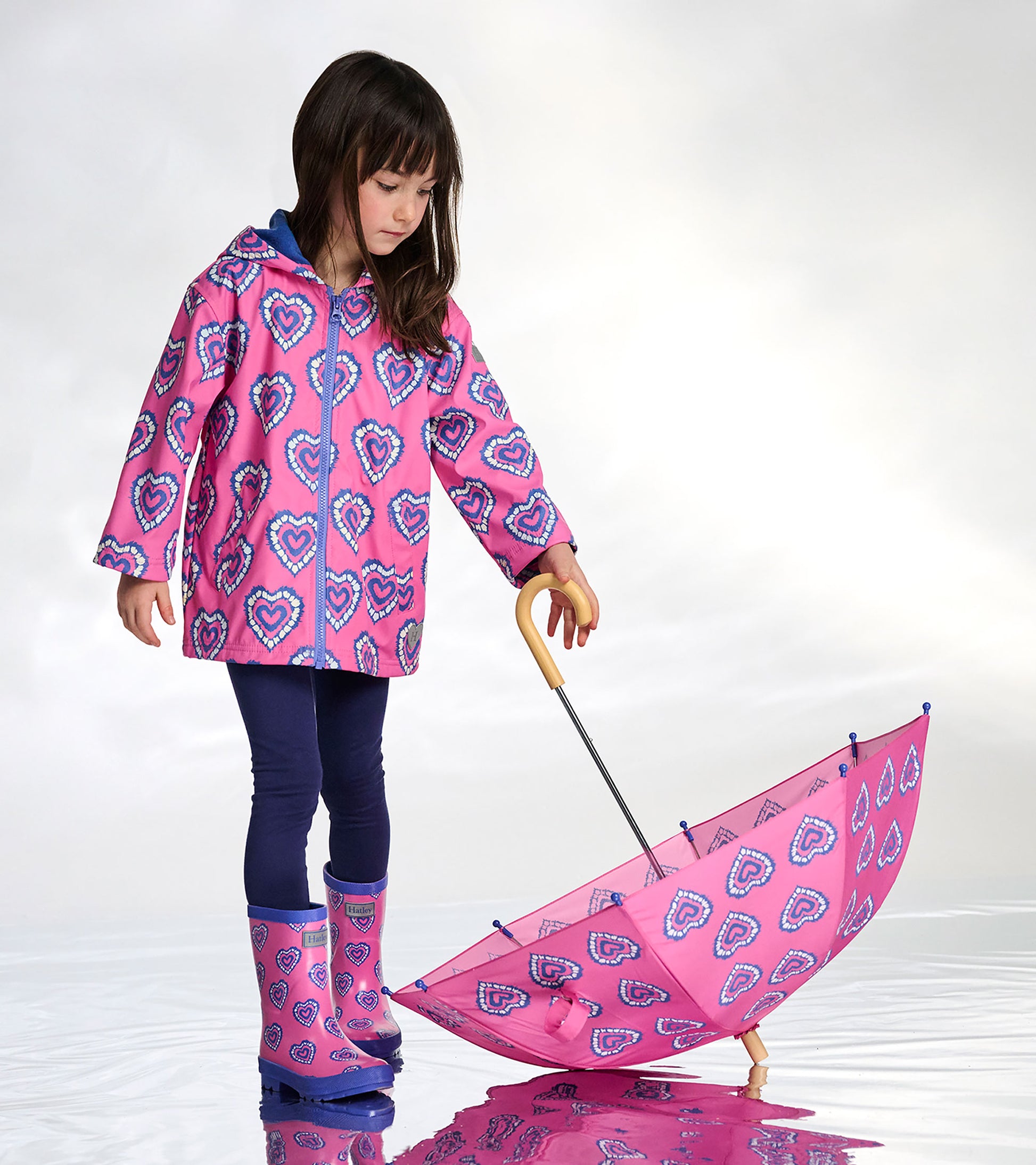 Pink kids umbrella with blue heart pattern, wooden handle, shown open with a child holding it