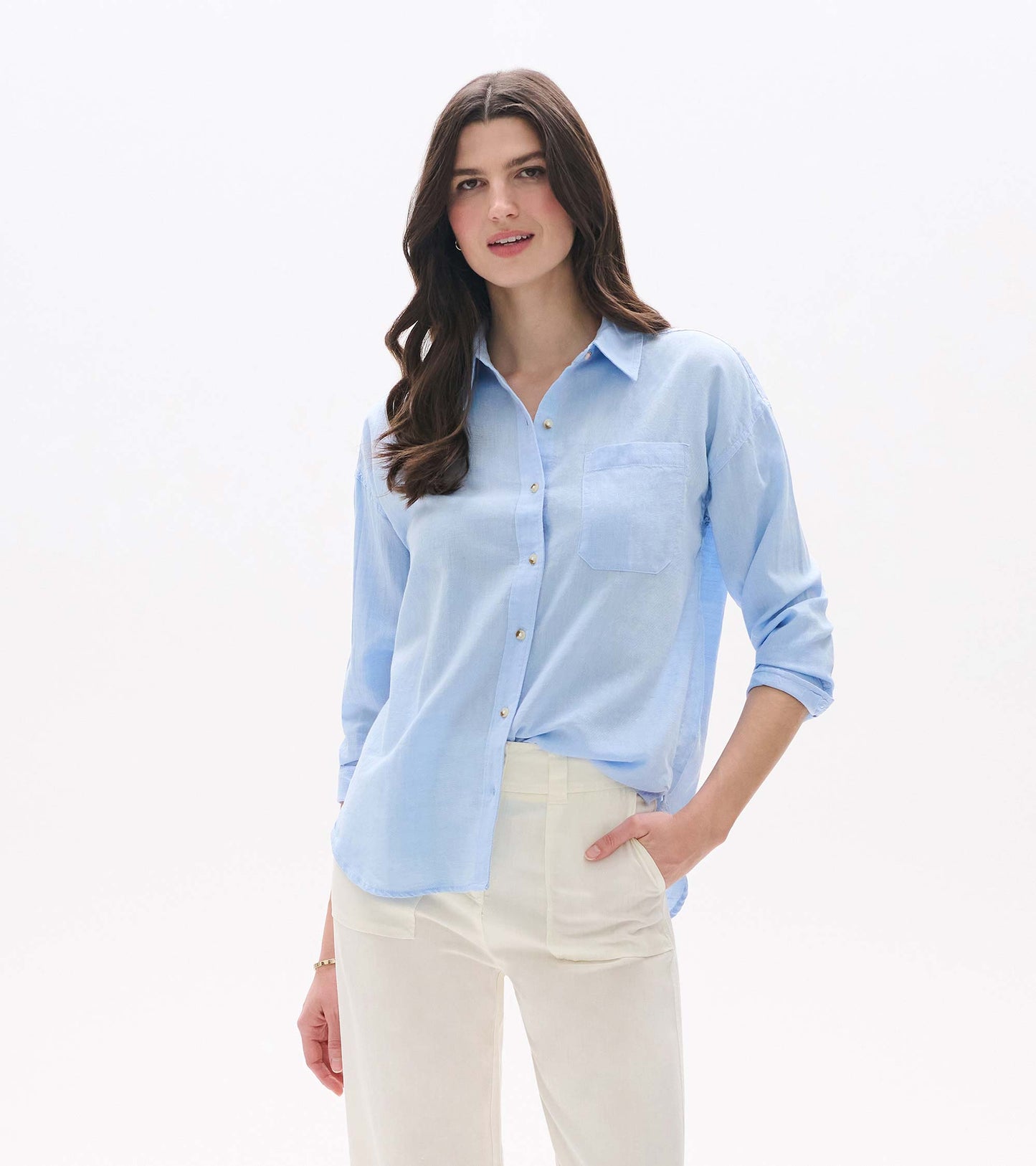 Light blue chambray button-down shirt with long sleeves, chest pocket, and relaxed fit, worn with cream pants.