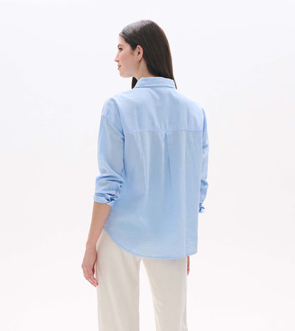 Light blue chambray button-down shirt shown from the back, with rolled sleeves and a relaxed fit.