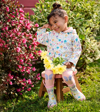 Pink rain boots with floral print and butterfly knee patches on a child sitting in a garden