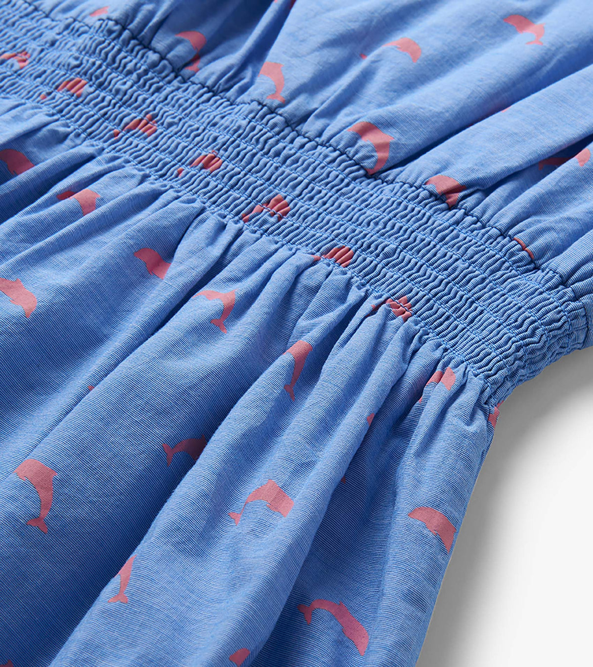 Close-up of blue dress smocked waistband with pink dolphin print and gathered skirt detail