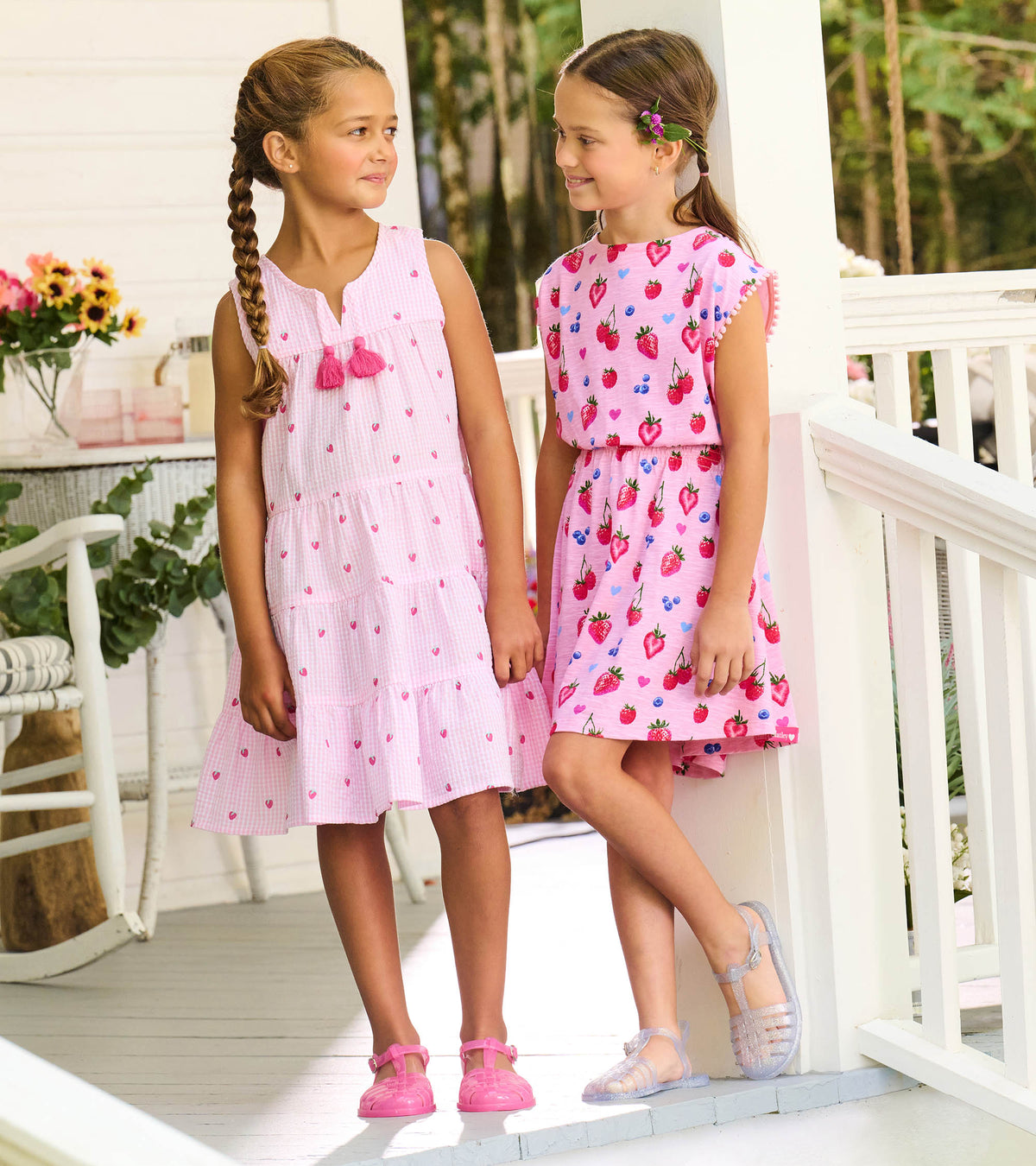 Girl wearing pink gingham berry print tiered dress beside another child on a porch