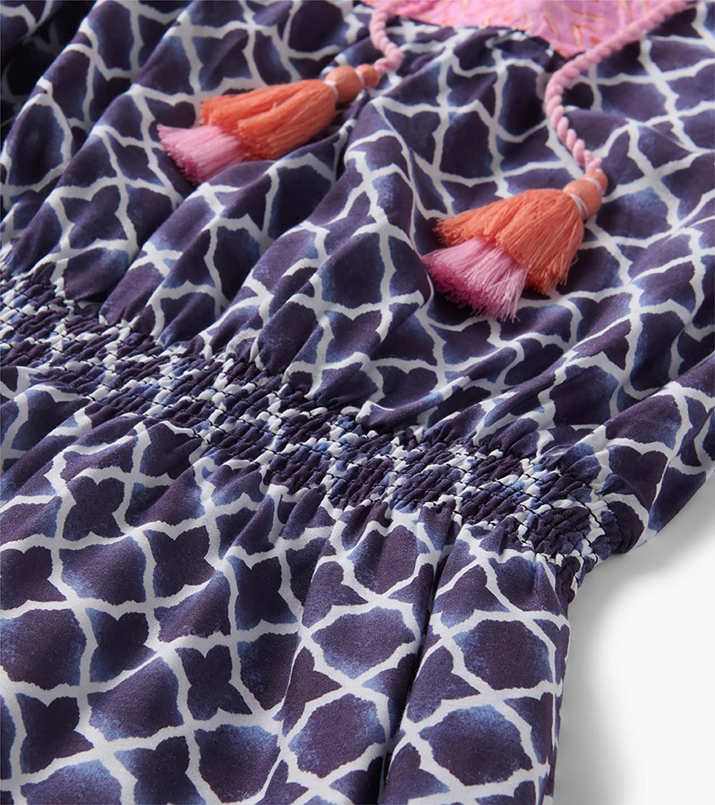 Navy and white patterned dress with pink-orange tassel ties and smocked waist detail, close-up view