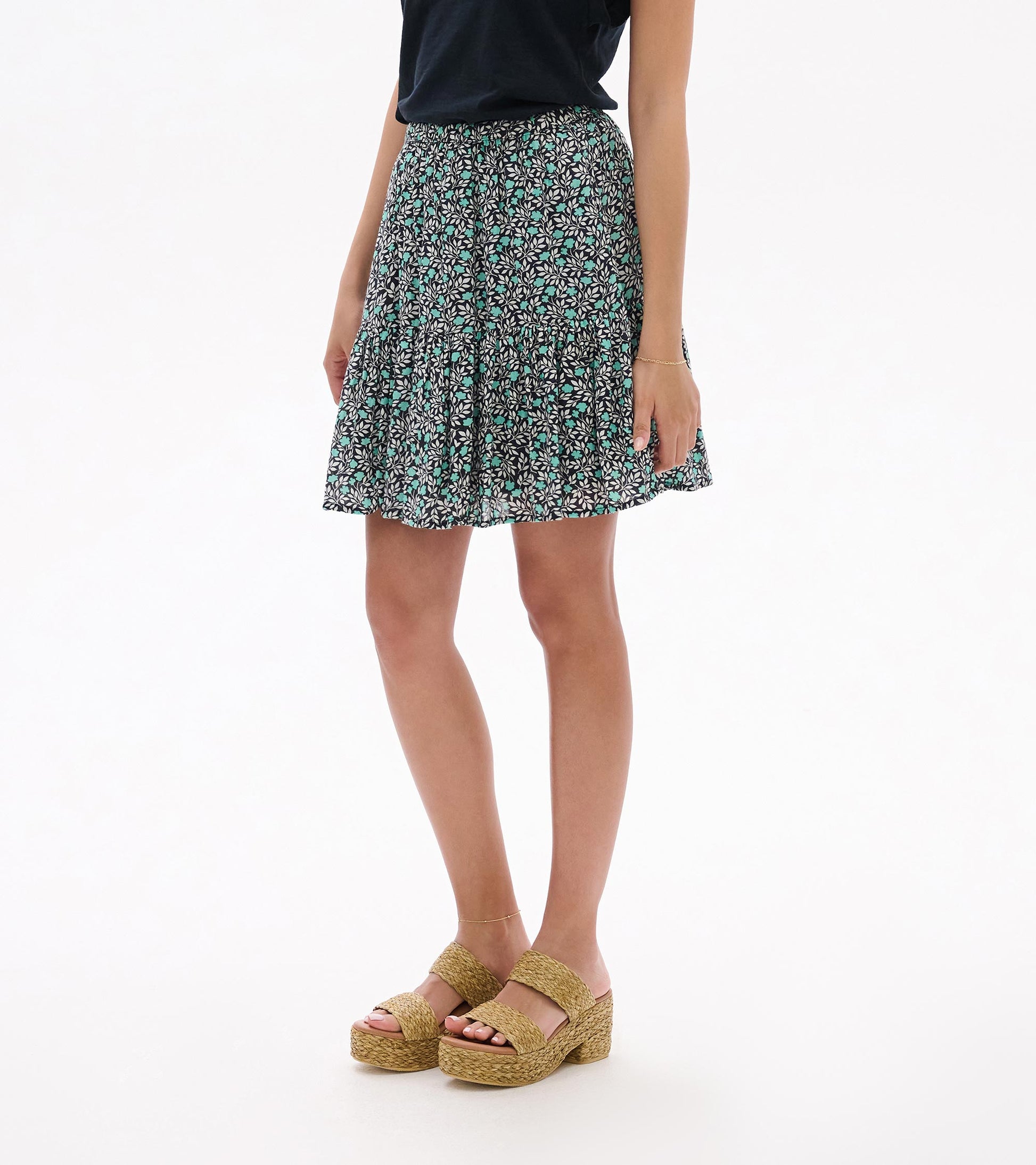 Mini flounce skirt with black, white and teal floral vine print, shown on model from front