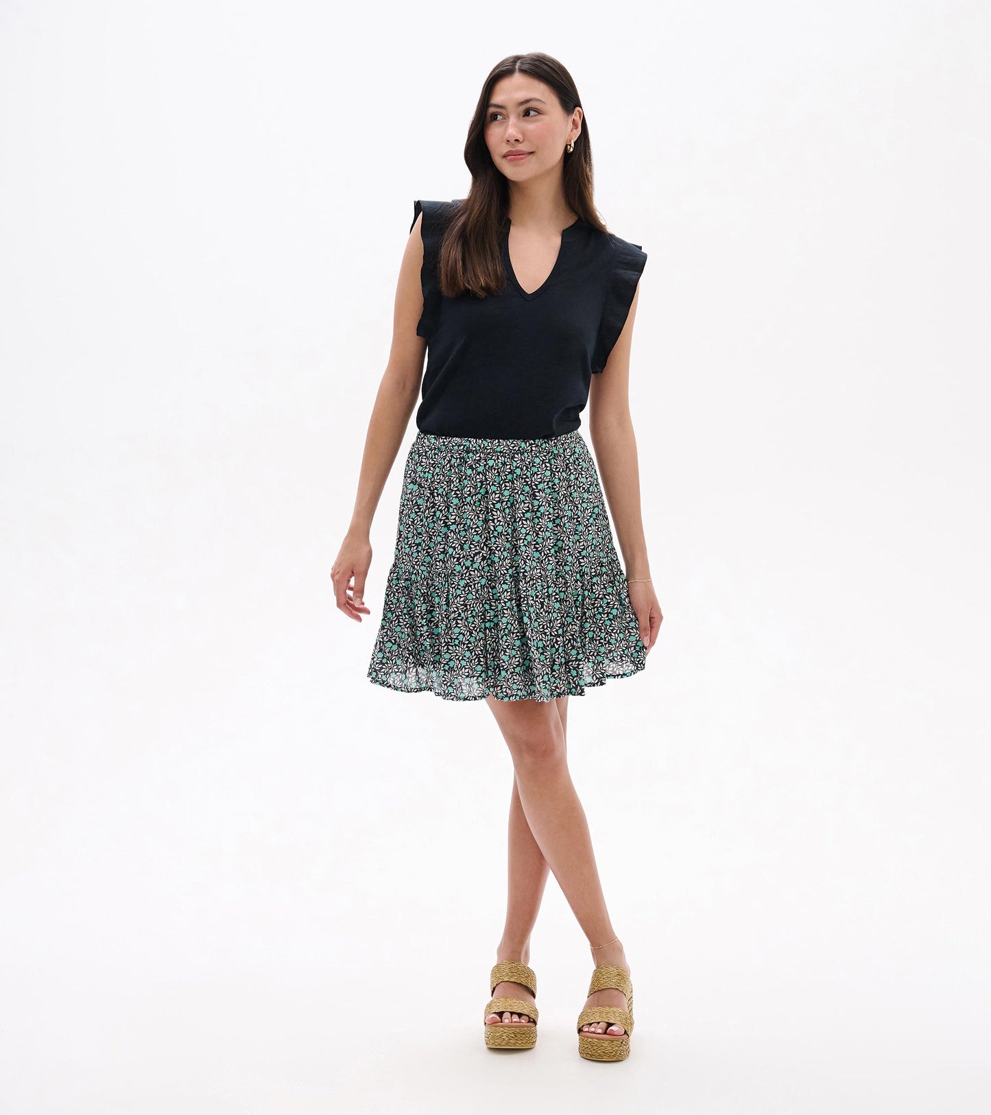 Woman wearing a black sleeveless top and a mini flounce skirt with teal and white vine print, front view