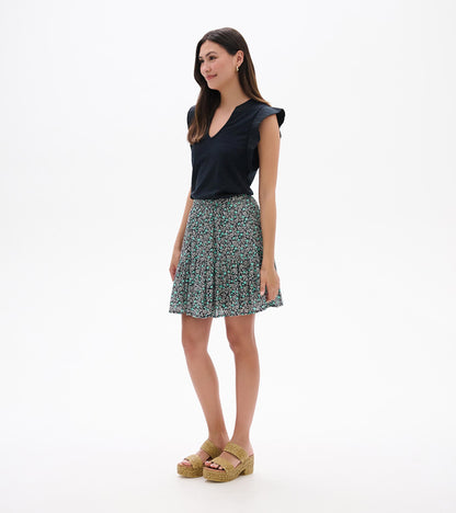 Woman wearing a black sleeveless top and a teal-and-black floral mini skirt with a flared hem, front view.