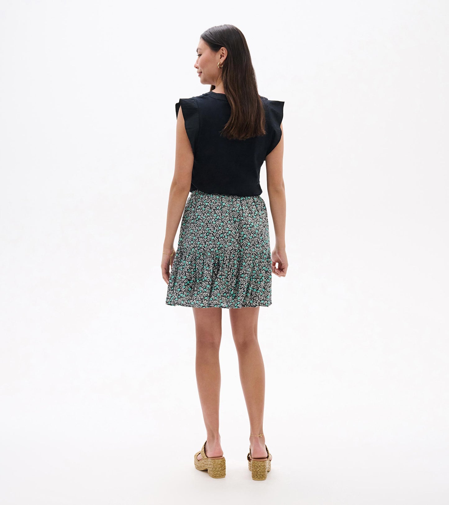 Back view of a black sleeveless top with a teal and white floral mini skirt and pleated hem