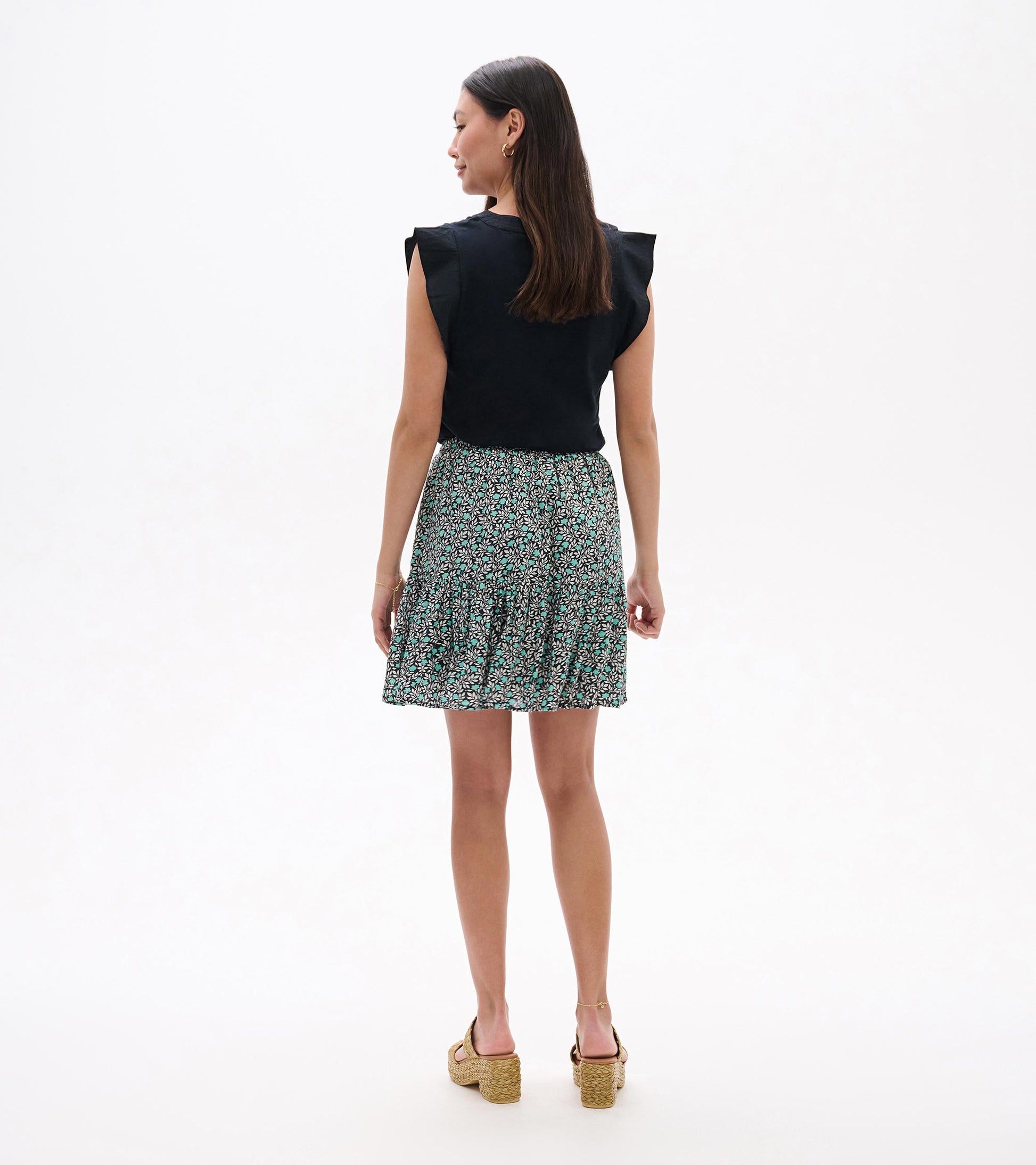 Back view of a black sleeveless top with a teal and white floral mini skirt and pleated hem
