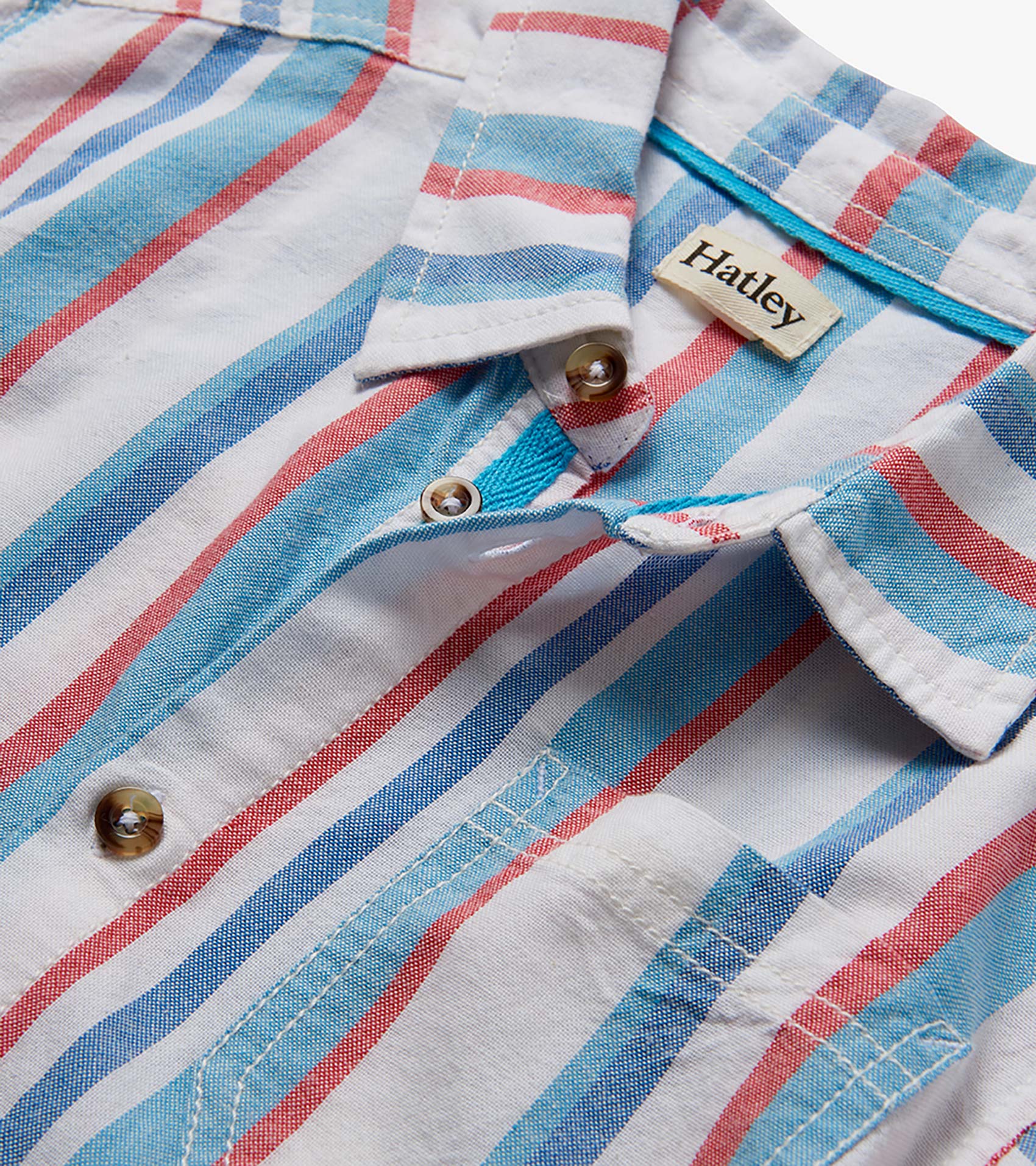 Close-up of a white woven button-down shirt with blue and red nautical stripes and brown buttons.
