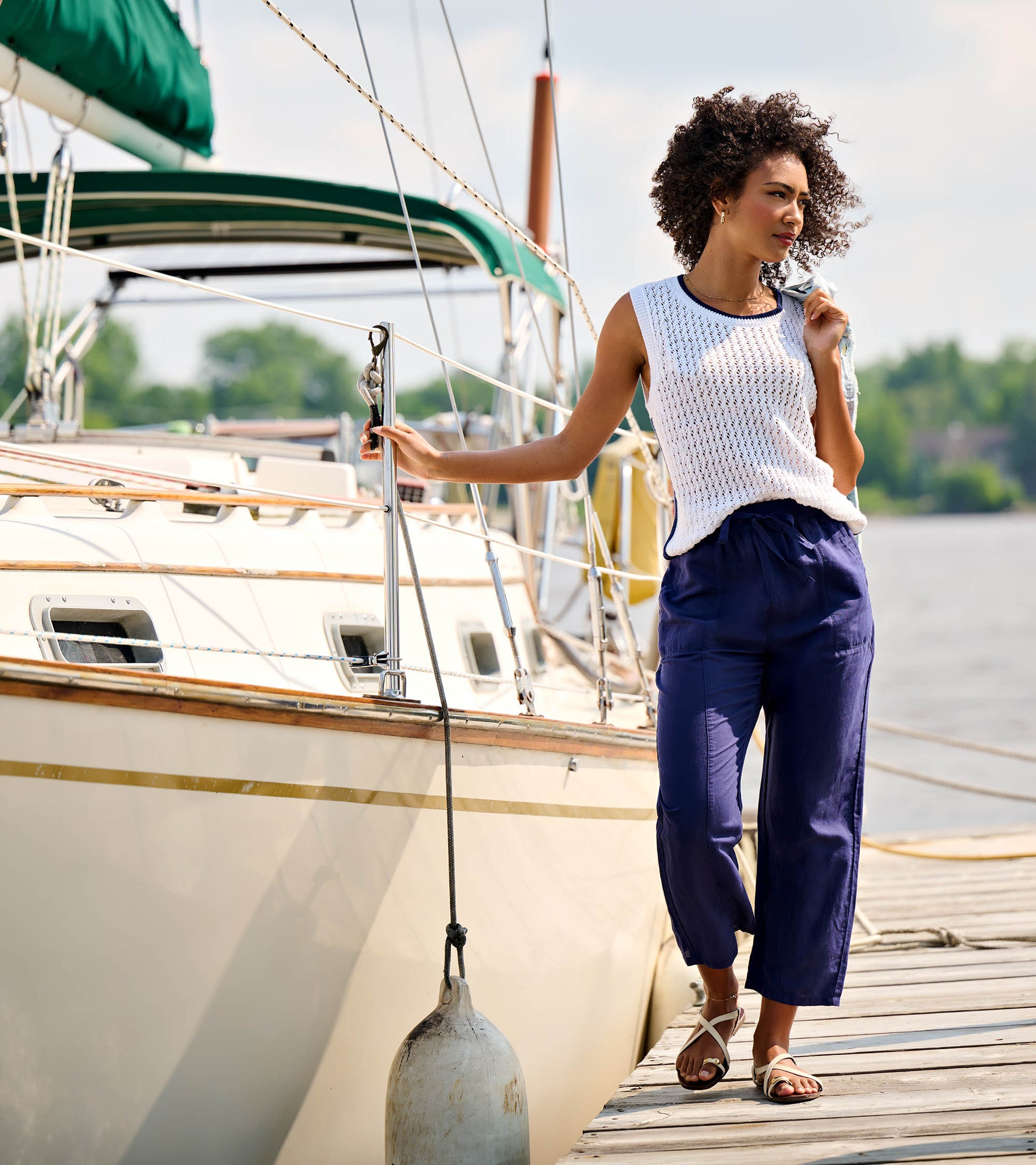 Woman wearing navy straight-leg pants on a dock beside a sailboat, paired with a white sleeveless top.