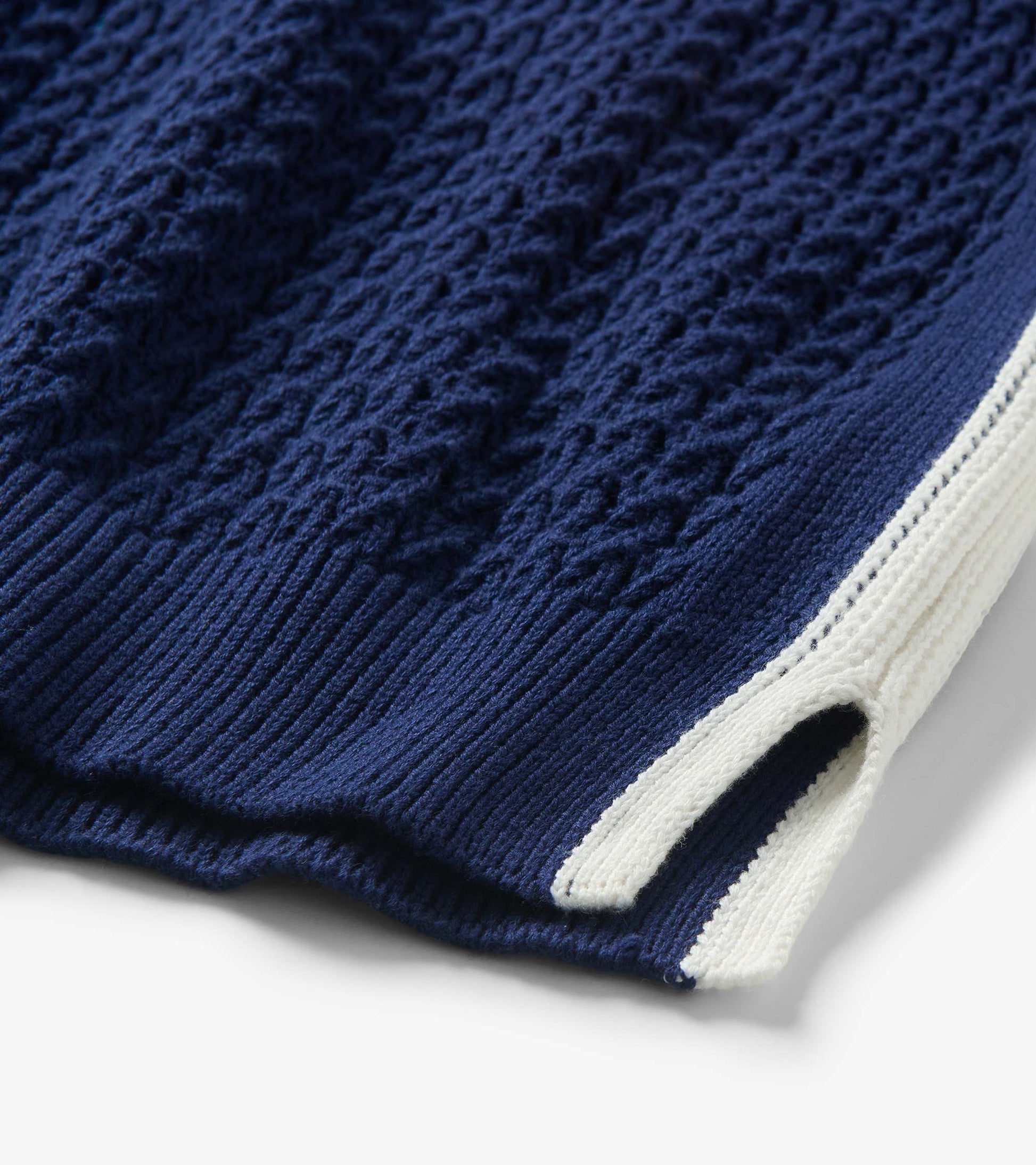 Close-up of a navy knit tank with textured cable pattern and white trim at the hem and armhole.