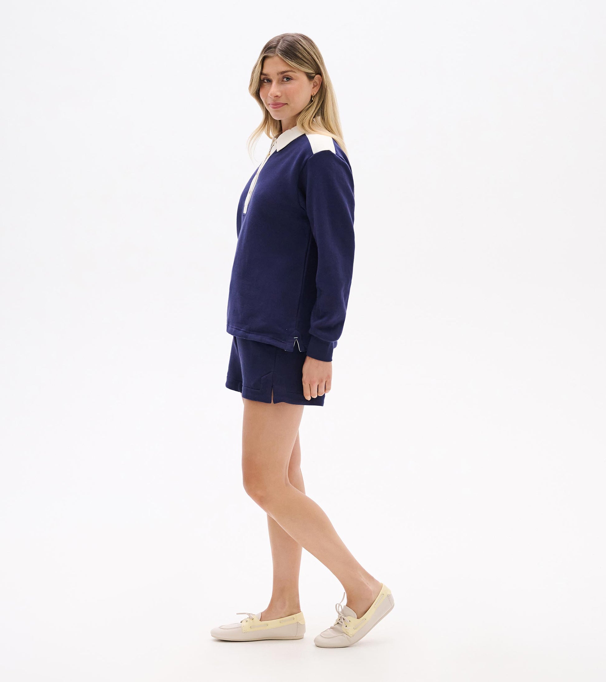Navy long-sleeve polo top with white collar and shoulder accents, shown on a model in side view.
