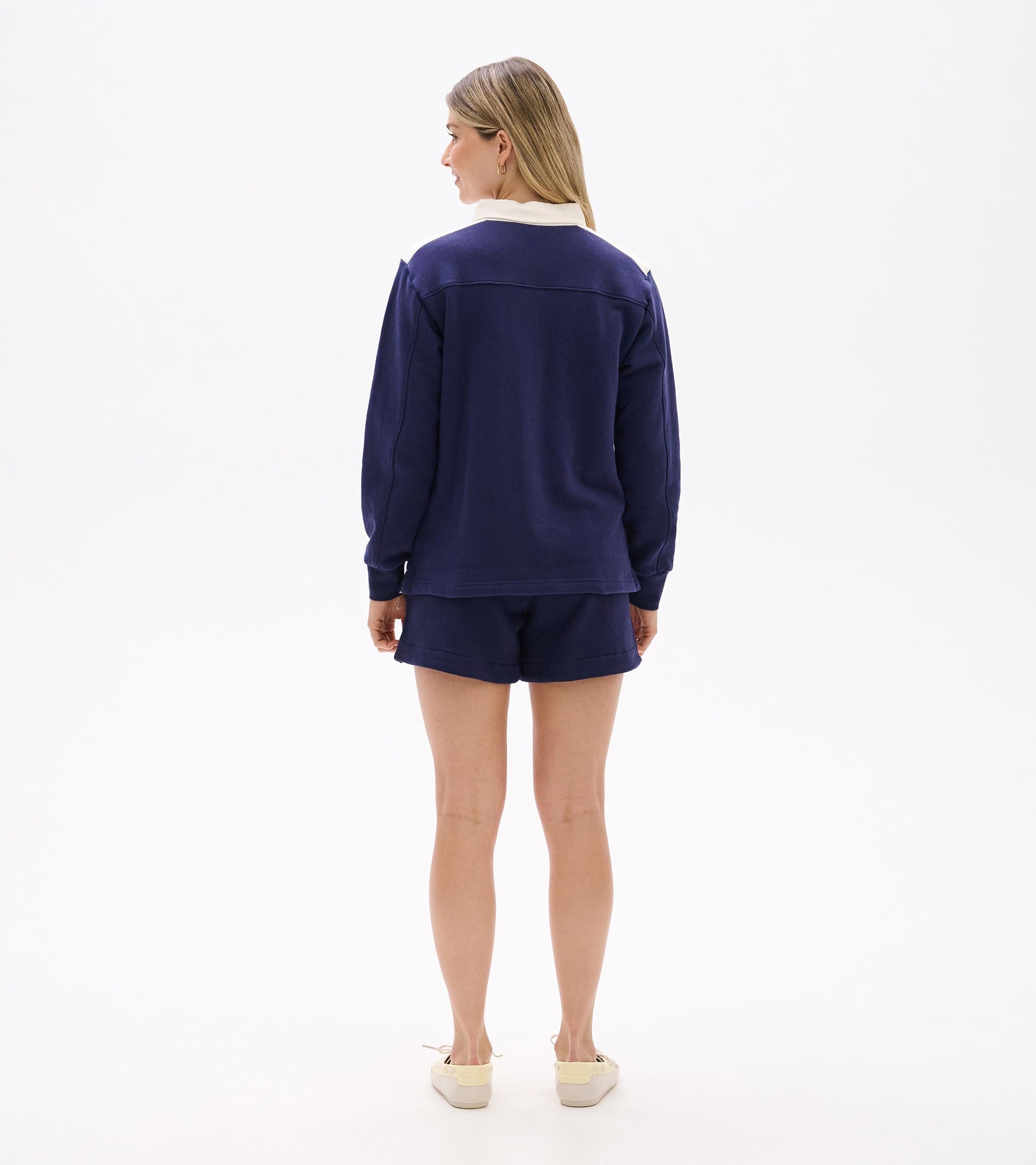 Back view of a navy long-sleeve top with white collar and shoulder panels, worn with matching shorts.