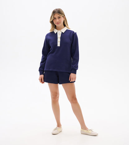 Navy long-sleeve polo top with white collar, placket, and shoulder accents, shown on a model front view.