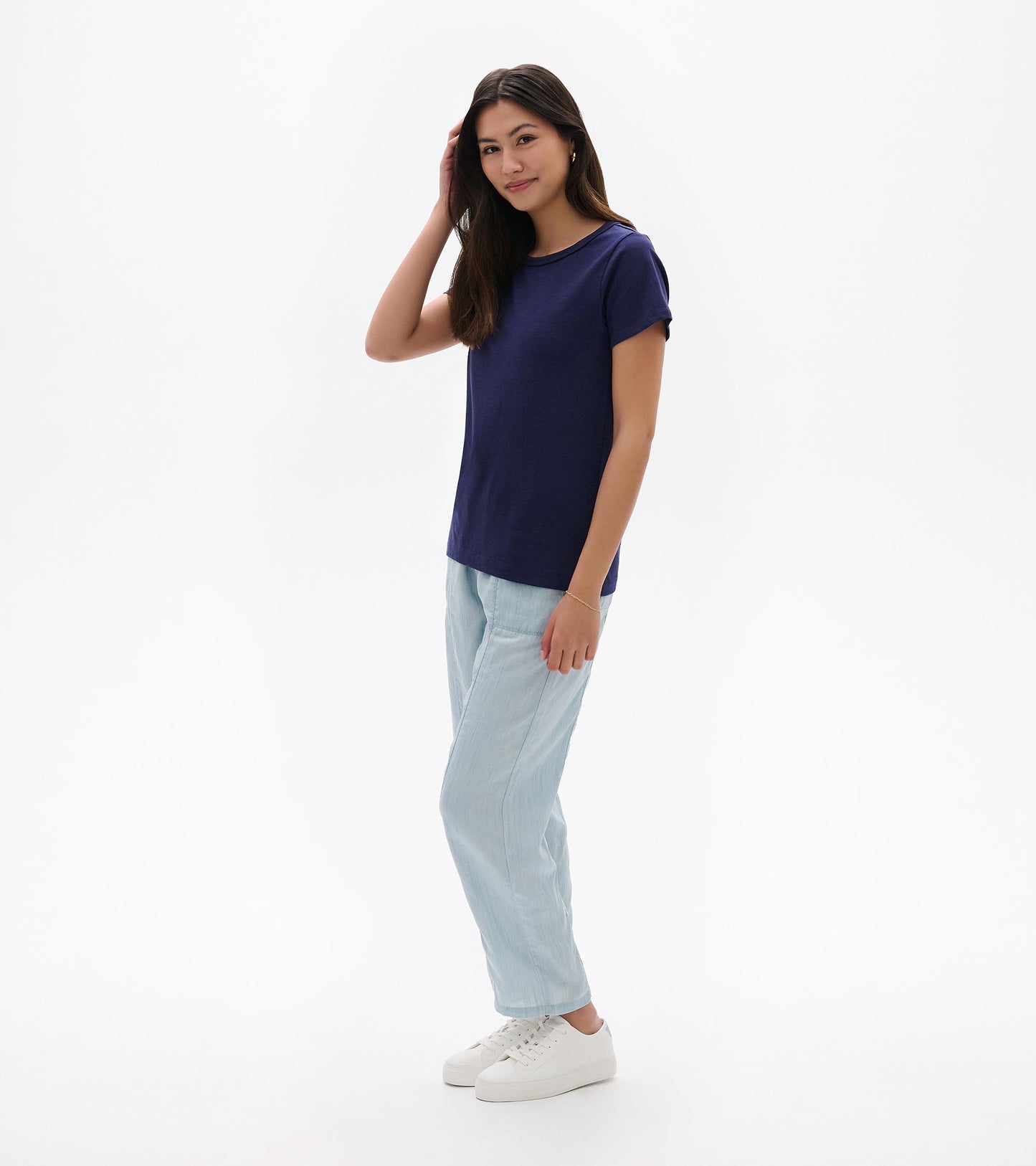 Woman wearing a navy crew neck short-sleeve tee with light blue pants and white sneakers, front view