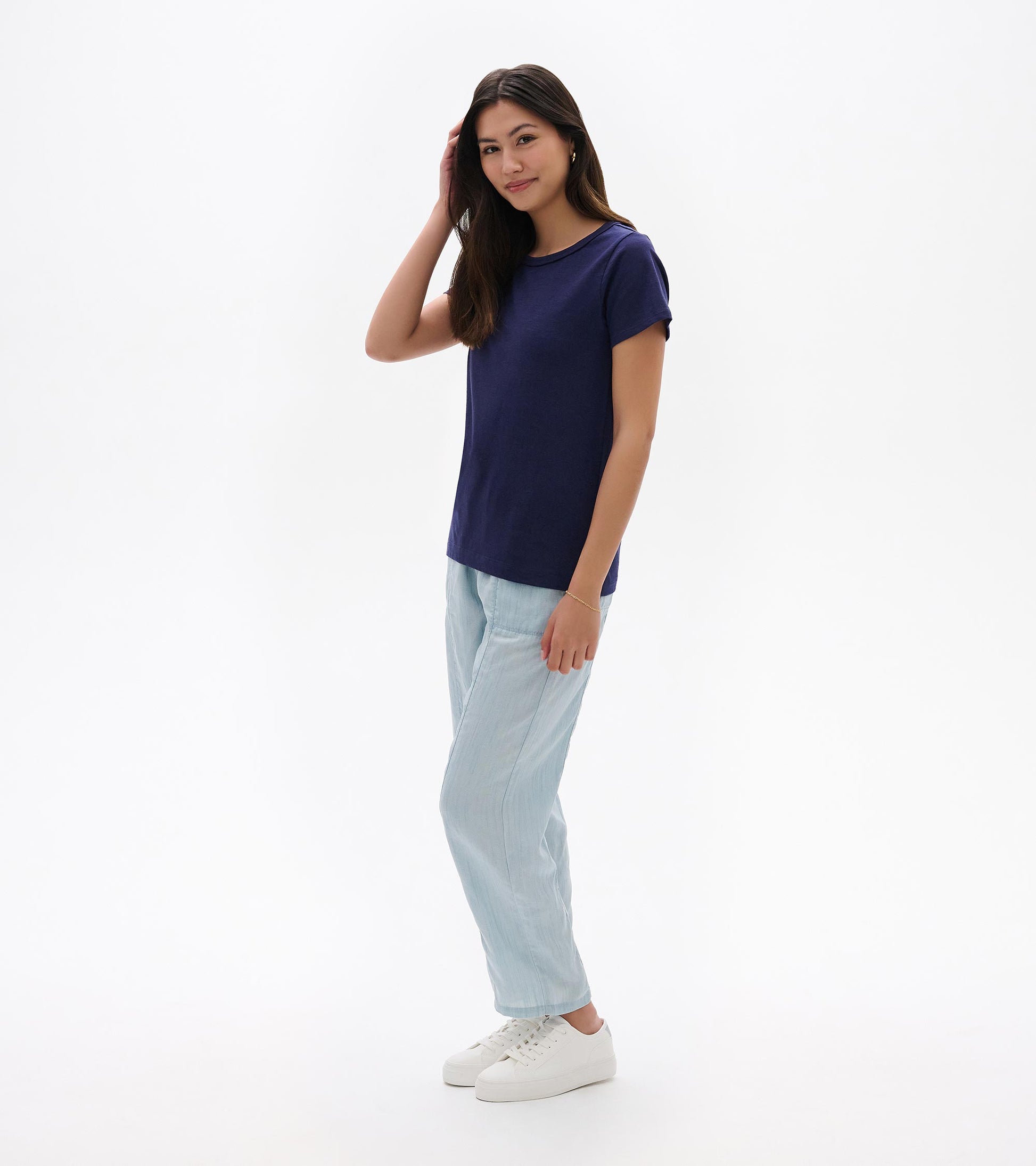 Woman wearing a navy crew neck short-sleeve tee with light blue pants and white sneakers, front view