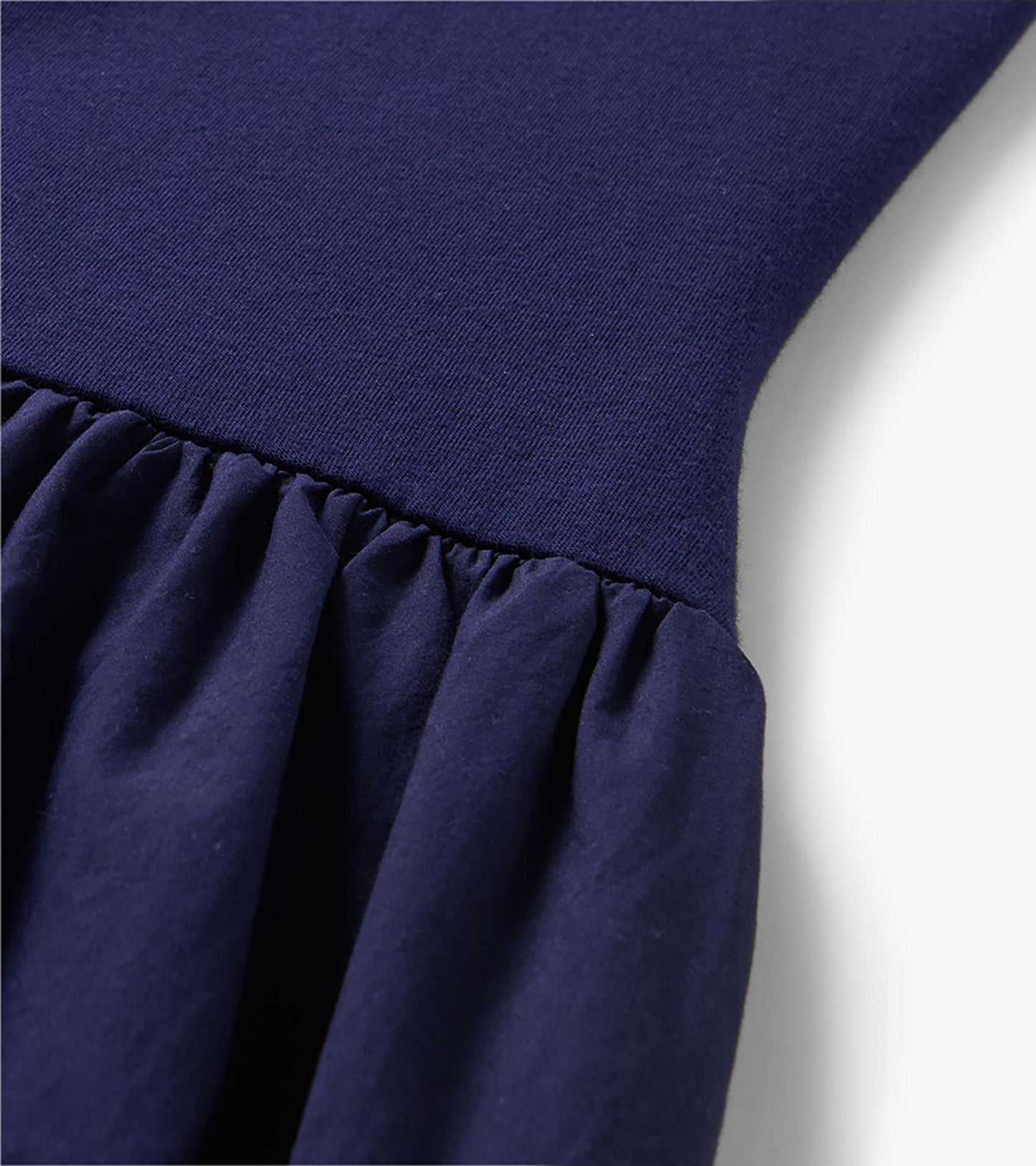 Close-up of a navy blue midi dress with a ribbed knit bodice and gathered ruffle skirt seam.