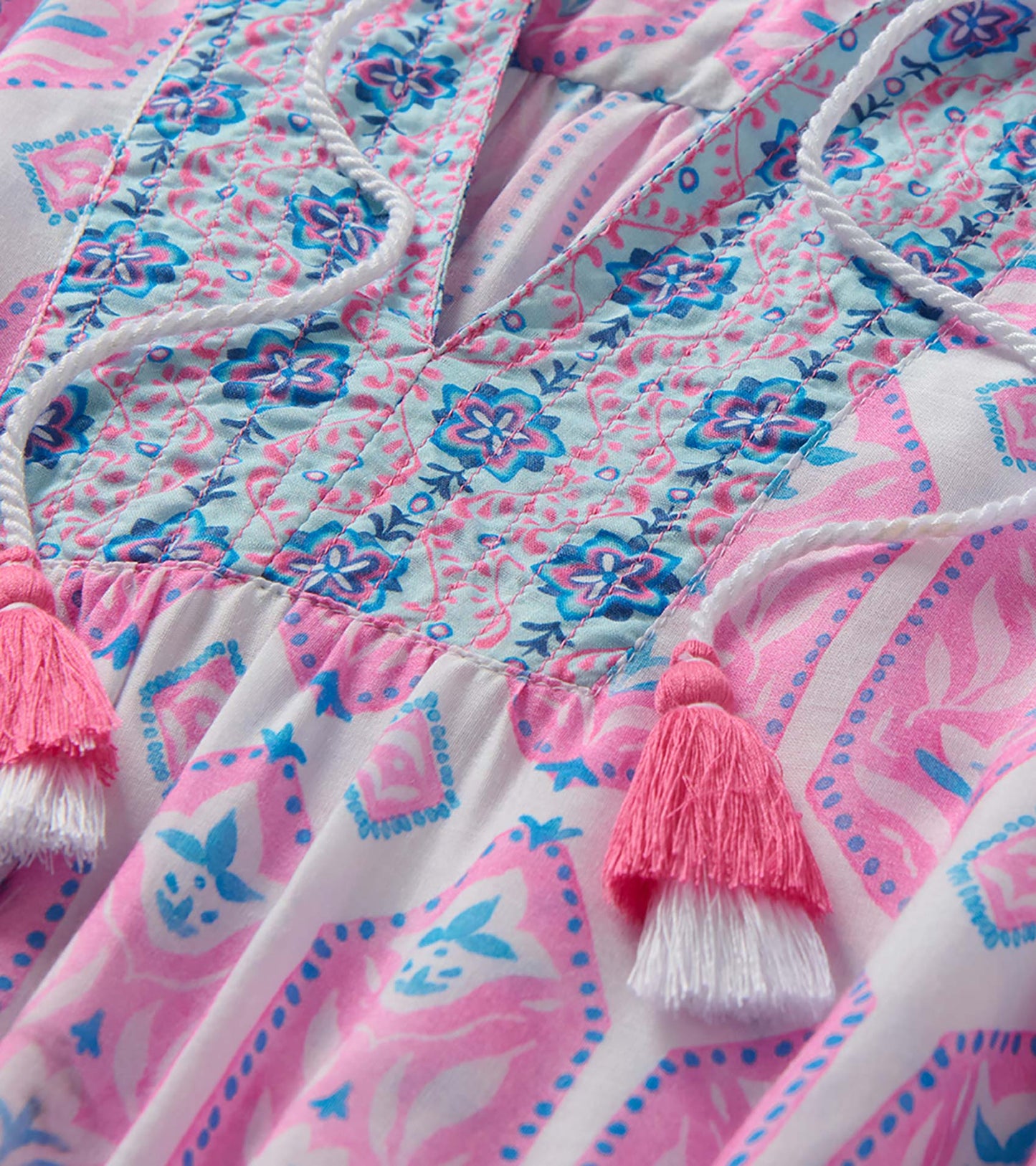 Close-up of the dress bodice with pink and blue floral print, quilted stitching, and tasseled tie neckline