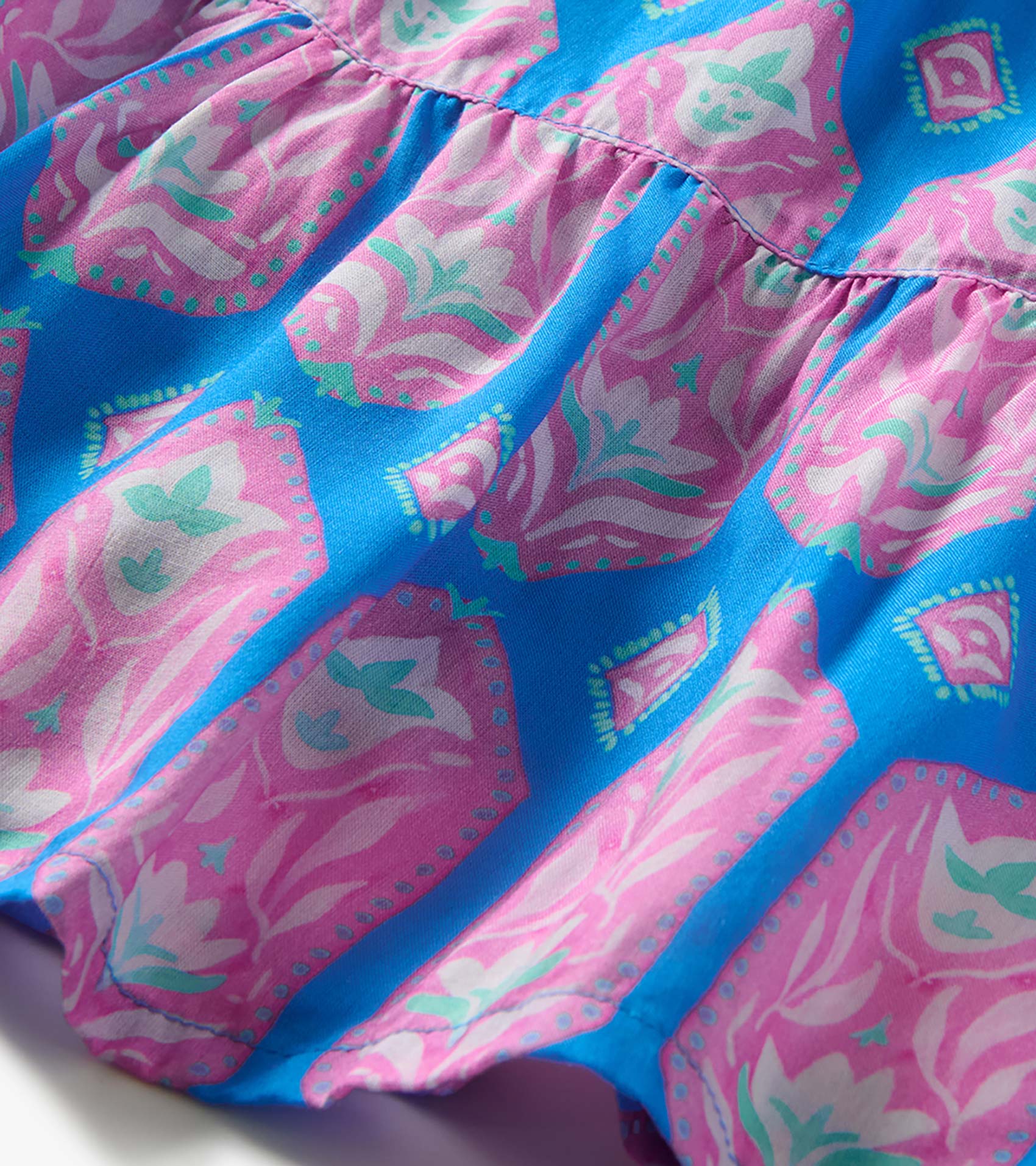 Close-up of gathered dress fabric with bright blue, pink, white, and mint floral geometric print
