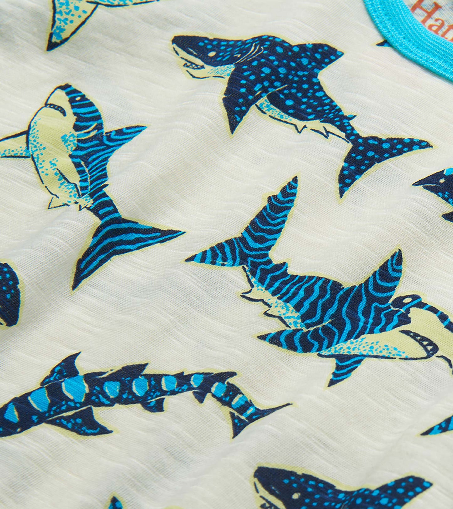 Close-up of white fabric with blue and teal shark print on a boys raglan T-shirt