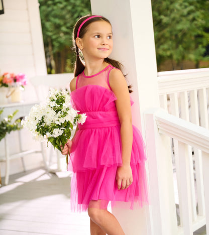 Side view of girl in a fuchsia tulle party dress with layered skirt, holding white flowers