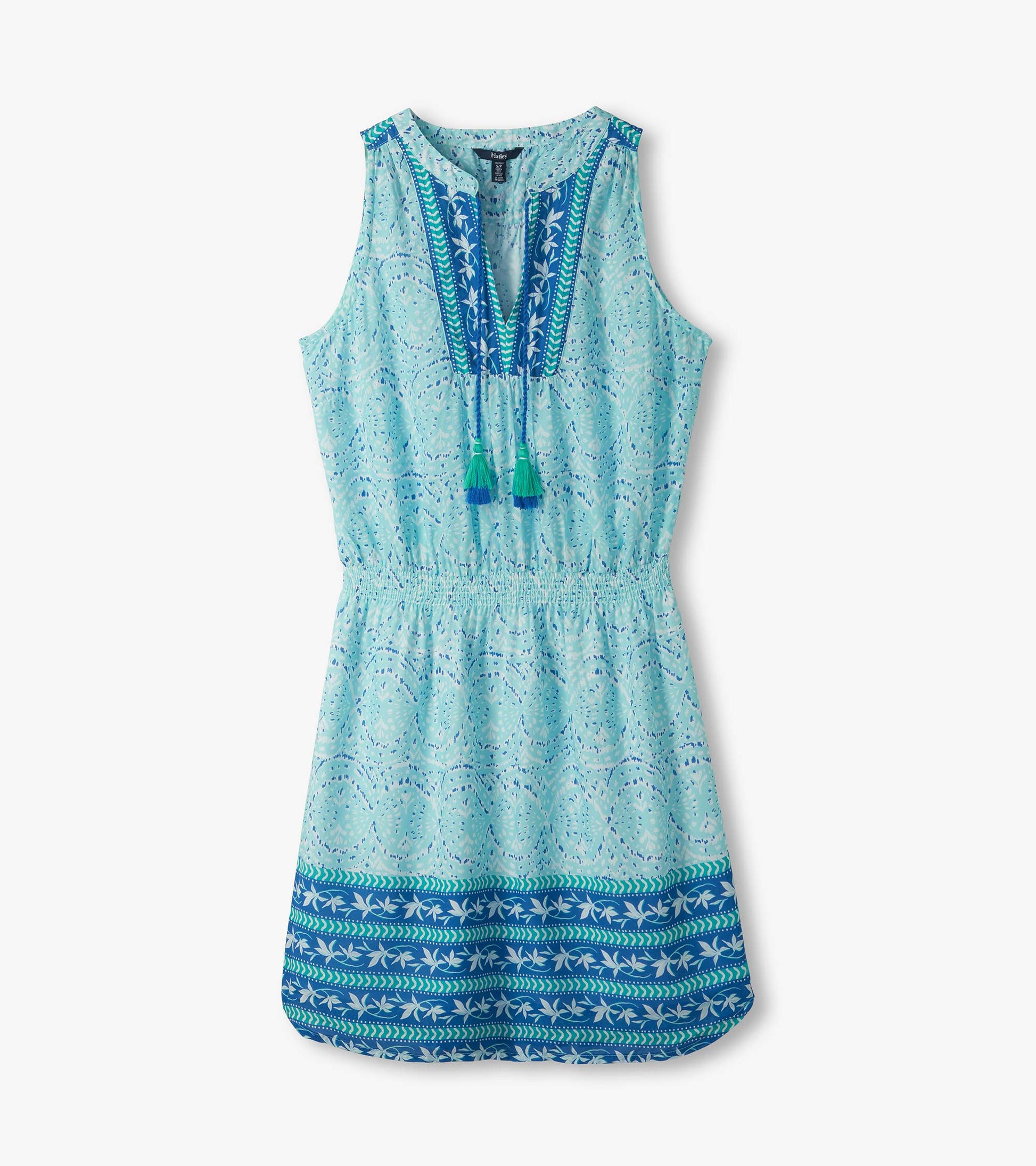 Flat lay of sleeveless beach glass ikat dress with tasseled split neckline, smocked waist and blue border hem
