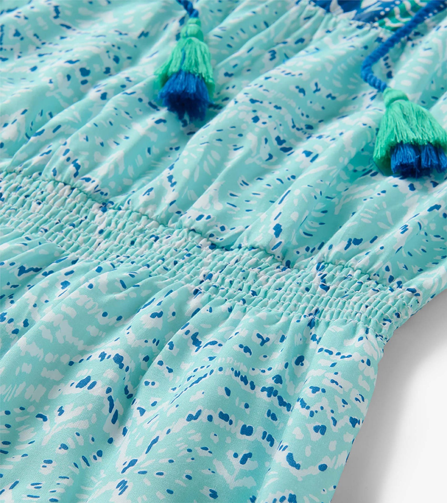 Close-up of Chloe Dress in beach glass ikat print with smocked waist and blue-green tassel ties