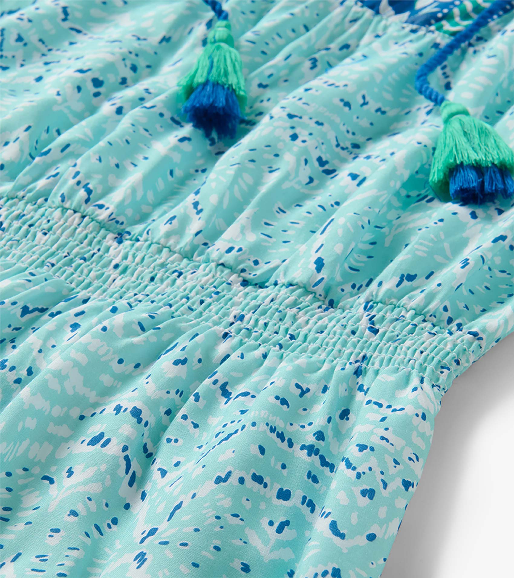 Close-up of Chloe Dress in beach glass ikat print with smocked waist and blue-green tassel ties