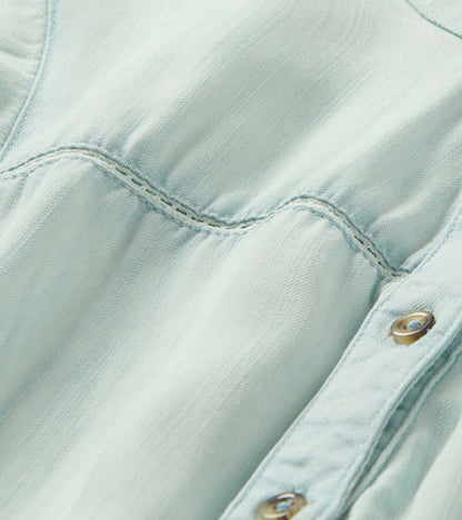 Close-up of a light blue denim dress with stitched seam detail and metal buttons